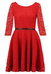 Robe rouge en dentelle à manches longues, col rond, taille cintrée avec une ceinture noire à clous, et jupe évasée. Motif floral texturé.