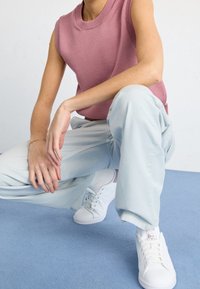 Light pink sleeveless knitted top paired with loose light blue pants and white sneakers against a blue background.