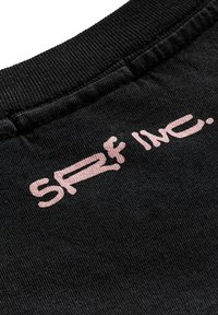 Czarna tkanina z prążkowaną teksturą, z logo "SRF INC." w jasnoróżowym haftowanym pisemnym stylu blisko górnej krawędzi.