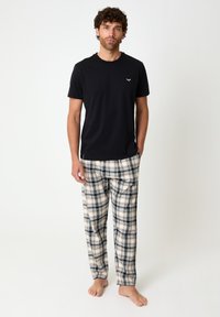 Black short-sleeve t-shirt with a small logo, paired with beige and black plaid flannel pajama pants, featuring an elastic waistband.