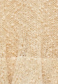 Dzianina w jasnym beżu, z otwartym wzorem koronkowym i teksturowanymi wypustkami, tworzy miękki, przewiewny wygląd.
