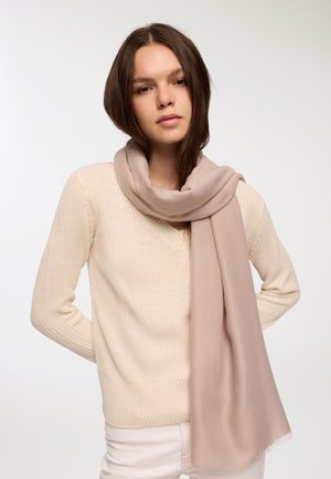 Maglione beige a maglia con scollo a V, abbinato a una sciarpa leggera beige, con texture, drappeggiata attorno al collo, caratterizzata da bordi sfilacciati.