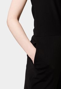 Mono negro con un diseño elegante y una textura suave, bolsillos laterales y una cintura ajustada, que muestra una estética minimalista.