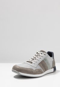 Szare zamszowe i materiałowe sneakersy z białymi sznurówkami, z dwoma zielonymi paskami oraz teksturowanym czubkiem. Gumowa podeszwa i wyściełana kostka.