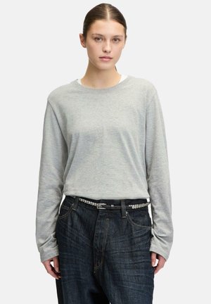 Langärmliges graues Shirt aus weicher Baumwolle mit Rundhalsausschnitt. Kombiniert mit dunkelblauen Jeans und einem schwarzen Gürtel mit silbernen Akzenten.