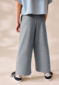 Pantaloni della tuta grigi a gamba larga realizzati in tessuto morbido. Abbinati a sneakers nere con logo bianco. Design semplice e casual.