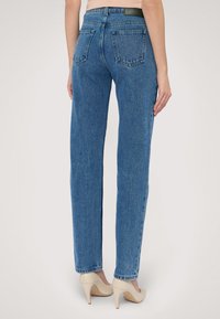 Modré džíny s rovnými nohavicemi, dvěma zadními kapsami a vysokým pasem, doplněné béžovými vysokými podpatky.