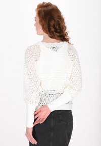 Maglione bianco lavorato a maglia con motivi texture, trama aperta e polsini a coste. Collo a scallop e dettaglio nero solido nella parte inferiore.