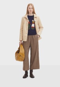 Giacca in corduroy beige sopra un maglione navy con lavorazione colorata. Pantaloni a quadri a gamba larga e stivali alla caviglia in pelle marrone. Borsa gialla.