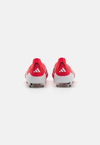 Des chaussures de football rouges avec une tige texturée, des accents blancs contrastants et un design épuré ; elles présentent trois bandes distinctes sur les côtés.