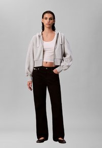 Grijs cropped sweatshirt met pofmouwen, wit tanktop, zwarte broek met wijde pijpen en zwarte platte schoenen. Eenvoudig ontwerp, zonder zichtbare patronen of accenten.
