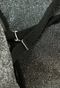 Metaliczno-szary materiał o teksturowej powierzchni, z czarnymi regulowanymi paskami i srebrnym metalowym zapięciem. Widoczne szczegółowe przeszycia.