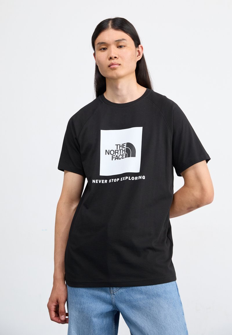 Camiseta de algodón negra con un gráfico cuadrado blanco que presenta el logo de "The North Face" y el texto "NEVER STOP EXPLORING" debajo. Manga corta.