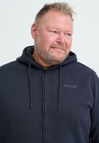 Felpa con zip di colore blu navy realizzata in tessuto morbido, dotata di cappuccio con cordino, zip frontale e logo "blend" in nero sul petto.