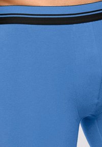 Tissu en coton bleu avec un design ajusté, doté d'une taille élastique noire avec deux bandes parallèles. Texture lisse, sans motifs visibles.