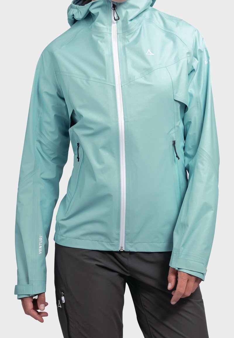 Veste imperméable bleu clair avec capuche, fermeture éclair frontale et deux poches latérales. Présente un design élégant et des poignets ajustables.