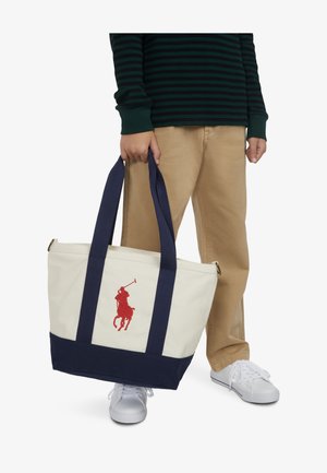 Torba na rame od krem platna s tamnoplavom podlogom i ručkama, s crvenim vezom logotipa igrača polom. Glatka tekstura, ležeran dizajn.
