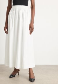 Jupe longue blanche en tissu léger, dotée d'une taille élastique et d'un design fluide. Associée à des talons aiguilles noirs.