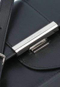 Borsa a tracolla in pelle nera con una texture liscia, hardware argentato e chiusura magnetica con la scritta "Lancaster" incisa. Include una tracolla.