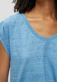 Modrý melange krátký rukáv top s kulatým výstřihem a jemnou texturou. Jemné variace v barvě vytvářejí uvolněný, lehký vzhled.
