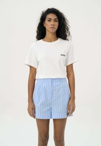 Biała bawełniana koszulka z krótkim rękawem, z małym czarnym logo. W połączeniu z niebiesko-białymi szortami w paski z wysokim stanem o gładkim wykończeniu.