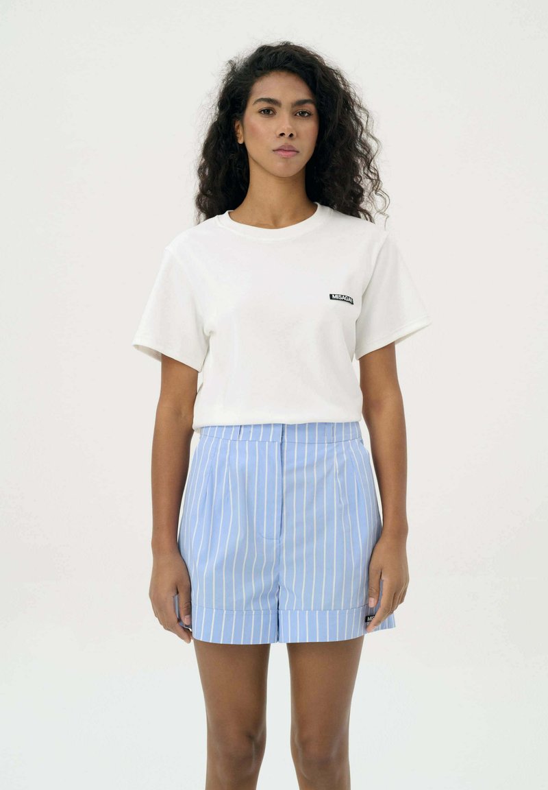 Biała bawełniana koszulka z krótkim rękawem, z małym czarnym logo. W połączeniu z niebiesko-białymi szortami w paski z wysokim stanem o gładkim wykończeniu.