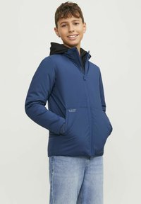 Mörkblå zip-up jacka med huva, med sidofickor och en texturerad inredning. Tyget ser slätt och något vadderat ut för värme.