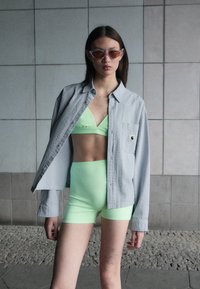 Ljusgrå texturerad knäppskjorta över en neongrön bikiniöverdel och matchande högmidjade shorts; slät tyg med livlig färgkontrast.