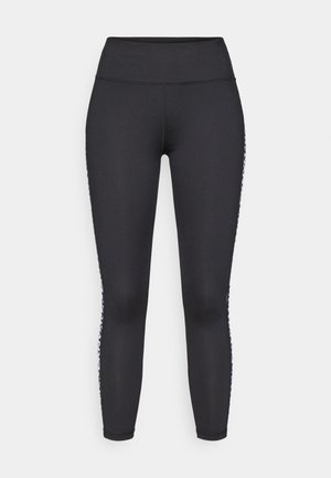 Črne dolge legice iz raztegljive tkanine, ki imajo gladek pas in bele vzorčaste dodatke vzdolž stranskih šivov.