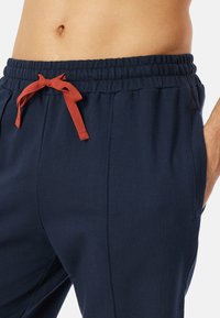 Marineblauwe sweatpants met een elastische tailleband, voorzakken en een contrasterend rode trekkoord. Gladde textuur met een relaxte pasvorm.