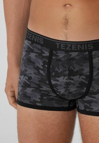 Černé a šedé maskáčové boxerky s černým elastickým pasem, na kterém je nápis "TEZENIS" šedou barvou. Tkanina má měkkou strukturu.