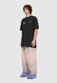 Melna kokvilnas t-kreklu ar īsām piedurknēm, uz kura ir balti un rozā teksta grafikas. Apvienots ar pastela gradienta platām biksēm un violetiem apaviem.