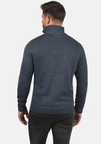 Dunkelblauer, gestrickter Pullover mit hohem Kragen, gerippten Bündchen und Saum. Verfügt über ein strukturiertes Muster und eine taillierte Silhouette am Rücken.
