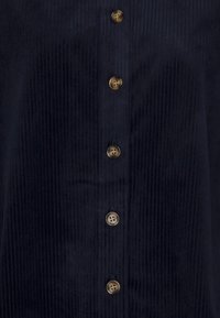 Camicia in corduroy blu scuro con texture a righe verticali, caratterizzata da sei bottoni dorati sul davanti e un design con colletto classico.
