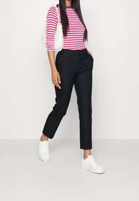 Pantaloni neri su misura abbinati a una maglia a maniche lunghe a righe rosse e bianche, completati da una borsa bianca testurizzata e sneakers bianche.