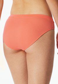 Bikini w kolorze brzoskwiniowym z prążkowanym wzorem i gładkim pasem, zapewniający okrągły kształt i średni wzrost, zaprojektowany z myślą o komforcie i wszechstronności.