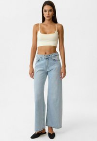 Lichtblauwe wijde jeans van denim, met een hoge taille en voorzakken. Gekleed met een crèmekleurige crop top en zwarte instapschoenen.