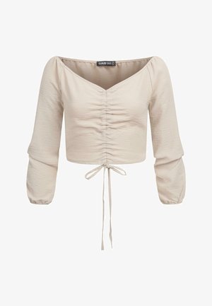 Világos bézs, cropped top, lekerekített dekoltázzsal, a frontján redőzött részletekkel és elasztikus puffujjakkal. Az alján húzózsinórral rendelkezik.
