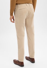 Beżowe spodnie sztruksowe o zwężanym kroju, z elastyczną talią i dwoma tylnymi kieszeniami, zestawione z brązowymi eleganckimi butami.