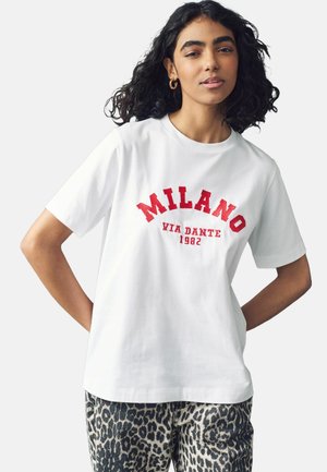 T-shirt en coton blanc avec des lettres en bloc rouges "MILANO VIA DANTE 1982", avec une coupe décontractée, associé à un pantalon imprimé léopard.
