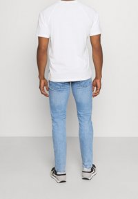 Vit kortärmad t-shirt med raglanärmar, kombinerad med ljusblå slim-fit jeans och svarta och beige sneakers.