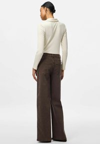 Långärmad ribbad topp i krämfärg som parats med högmidjade bruna vida jeans, med bakfickor och en avslappnad passform.