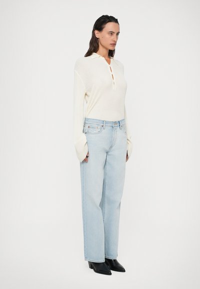 Maglione a coste color avorio con colletto, apertura con bottoni, abbinato a jeans a gamba larga blu chiaro e stivaletti neri con punta.