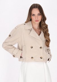 Beige dobbeltradet cropped jakke lavet af bl�ødt stof med store knapper, slagkrave og sidelommer. Ensfarvet baggrund.
