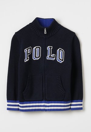 Chaqueta azul marino de punto con cremallera, cuello de canalé, puños y dobladillo a rayas en azul y blanco, bolsillos frontales y letras "POLO" en el pecho.