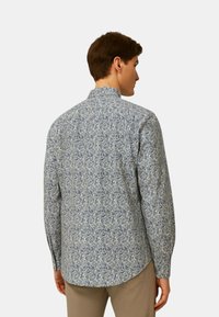 Camicia a maniche lunghe in tessuto azzurro chiaro con un motivo floreale. Collo classico e polsini con bottoni. La vista posteriore mostra l'orlo curvato.