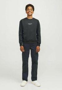 Felpa nera con collo rotondo e logo bianco sul petto, abbinata a pantaloni cargo in blu scuro e sneaker bianche. Outfit semplice e casual.