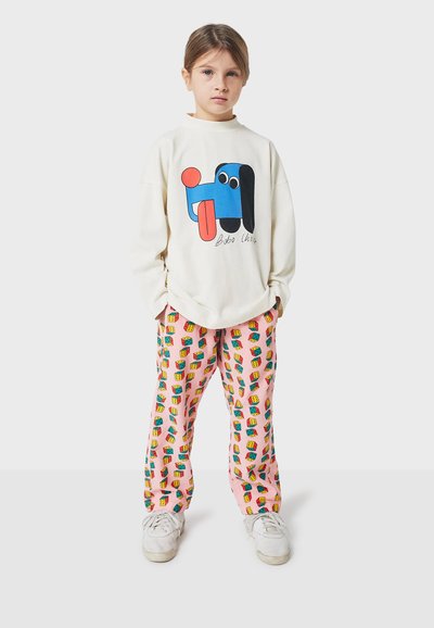 Sweatshirt blanc avec un graphique d'un chien bleu et d'une balle rouge, associé à un pantalon rose avec des motifs de maisons colorées. Des baskets blanches complètent le look.
