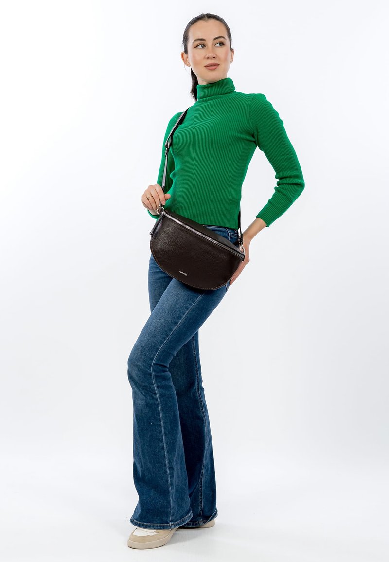 Žali, iškiliais raukšlėmis puoštas golfas, išplatėję mėlyni džinsai ir kreminės spalvos sportbačiai. Laiko tamsiai rudos odos rankinę per petį su užtrauktuku.