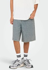 Shorts de mezclilla azul claro con un patrón texturizado, corte clásico y bolsillos laterales, combinados con una camiseta blanca y zapatillas deportivas grises.